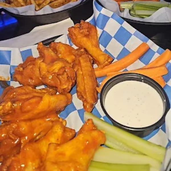 Hot Pockets Sports Bar's buffalo wings with carrots, celery, and ranch dressing on blue checkered paper.