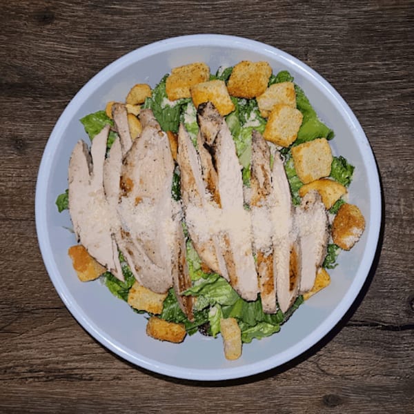 Grilled chicken Caesar salad with croutons and parmesan cheese on a light blue plate.